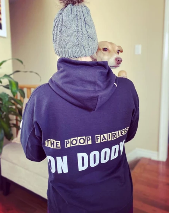 A founder wearing a purple Poop Fairies 'On Doody' hoodie, holding a small dog